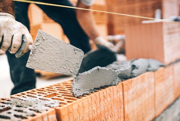 Masonry Contractor Insurance - Close-up of Construction Worker With Protective Gear and Trowel and Mortar Building Brick Walls