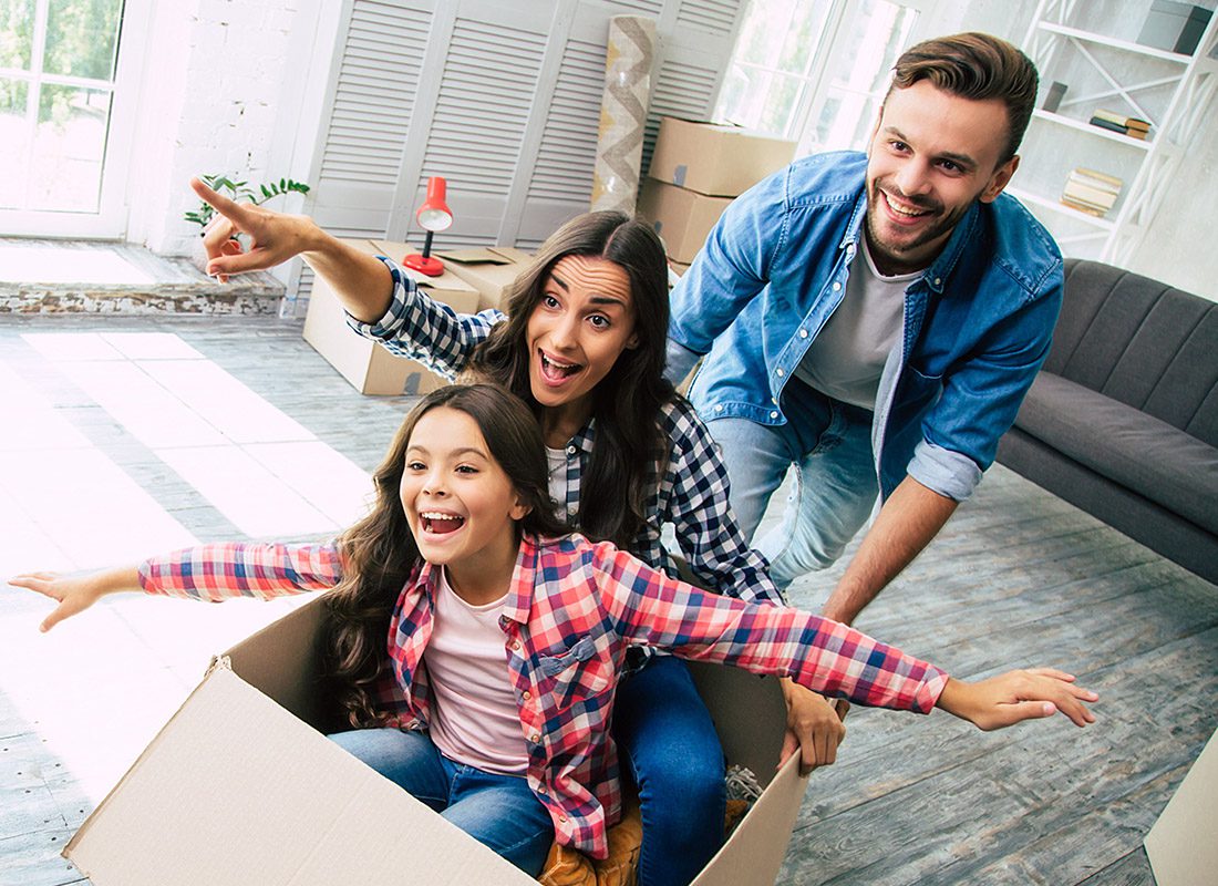 Personal Insurance - Happy Father Pushes Mother and Daughter as They Sit Inside a Cardboard Box During Moving Day at Their New Home